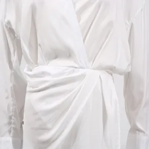 Macro detail view of elegant white V-neck midi dress featuring unique twisted waist design