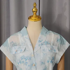 Détail d'une robe chemise bleu clair à imprimé palmier tropical et boutons perlés.