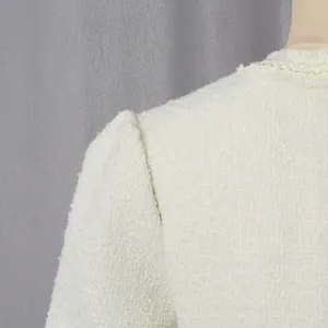 Detailaufnahme eines cremefarbenen Tweed-Kleides mit strukturierter Textur und Fransenrand