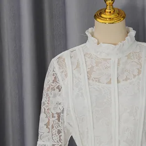 Detailed view of an elegant white lace dress with high ruffle neck and floral motifs