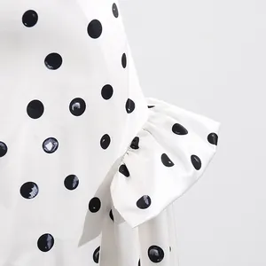 Detailed close-up of a white satin skirt featuring black polka dots and an elegant ruffle fold