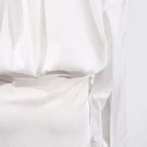 Close-up view of the elegant pleats and buttoned cuff on a white high-waist dress for women.