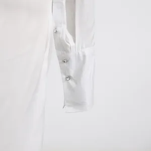Detail view of a white dress sleeve cuff featuring elegant sparkling crystal buttons.