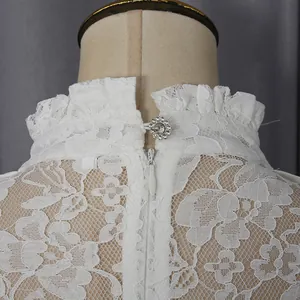 Detail view of white lace dress featuring high ruffled collar and crystal button.