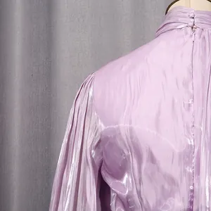 Detail of lilac pleated dress featuring a high neck with button and zipper closure