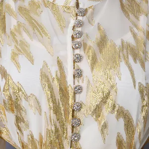 Close-up of elegant gold embroidery and crystal rhinestone buttons on a summer dress detail.