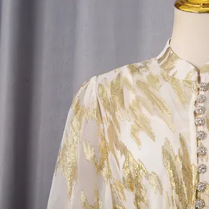 Detailed close-up of an elegant white summer dress featuring gold embroidery and rhinestone buttons