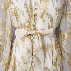 Close-up of white summer dress featuring gold leaf patterns and sparkling crystal buttons