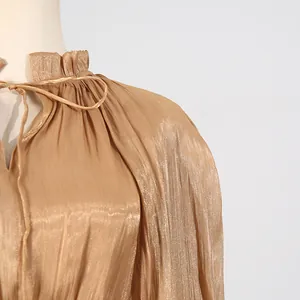 Detail of champagne pleated dress showing ruffled collar and tie-up neckline.