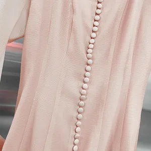 Close-up detail of an elegant pink pleated dress showing decorative fabric-covered buttons