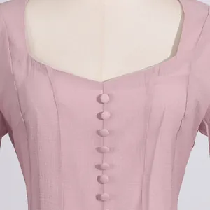 Detalle de primer plano de un vestido rosa de verano con escote cuadrado y botones decorativos.