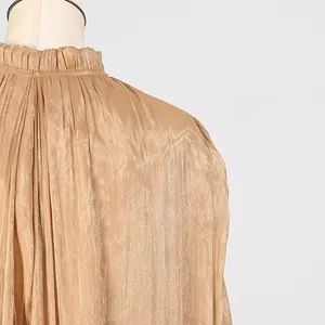 Close-up of elegant pleated champagne gold dress featuring a ruffled high neckline.