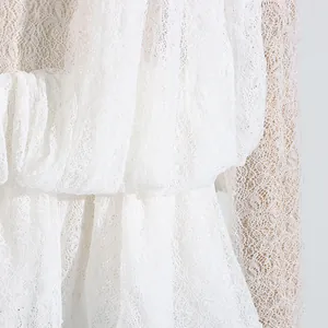 Nahaufnahme der filigranen weißen Spitzenstruktur und der Volants an einem Netzkleid