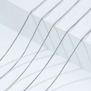 Detail of multiple silver stainless steel snake chains on minimalist white blocks.