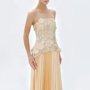 Close-up of elegant strapless top with 3D floral embroidery and pleated maxi skirt in peach