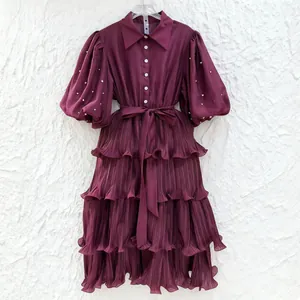Detailed view of burgundy French-style tiered pleated dress with pearl-embellished puff sleeves