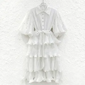 Detailed view of white tiered dress with puff sleeves and sparkling rhinestone accents.