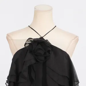 Close-up detail of a black halter dress with a large fabric rose and ruffled layers