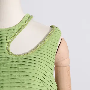 Detalle de blusa plisada verde lima con escote recortado adornado con pedrería