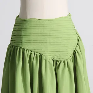 Detalle de una falda verde con cintura plisada e intrincados pliegues horizontales.