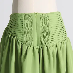 Detalle de falda plisada verde con cintura fruncida y cremallera invisible