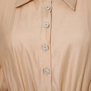 Detailed view of elegant rhinestone buttons on a champagne satin French style dress fabric.