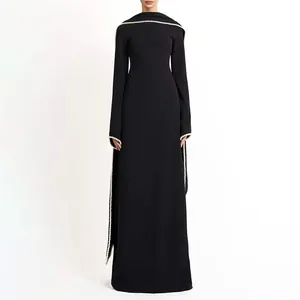 Detail of an elegant black long dress with white pearl trim and cape design.