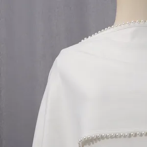 Detail shot of white evening gown featuring elegant pearl trim along the shawl edge