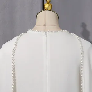 Close-up detail of a white elegant dress featuring a pearl-embellished neckline and zipper
