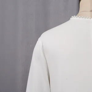 Detailed macro view of the elegant pearl-embellished neckline on a white French style dress.