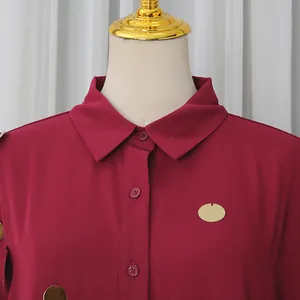 Detalle de camisa burdeos de manga larga con lentejuelas doradas y cuello con botones.