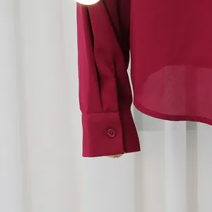 Primer plano del puño de una camisa burdeos con detalle de botón a juego.