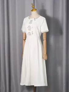 Elegant white midi dress with rhinestone neckline and bow detailing on wooden mannequin