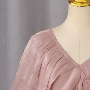 Gros plan sur l'encolure en V plissée et le tissu soyeux d'une robe longue rose romantique