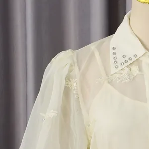 Vista detallada de un elegante vestido crema con mangas abullonadas y cuello de pedrería