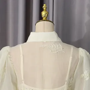 Vista detallada del elegante bordado de hojas en la espalda transparente del vestido crema de moda