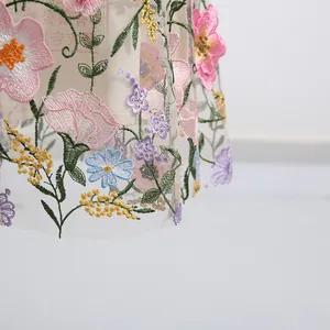 Close-up van fijn veelkleurig bloemenborduurwerk op elegante doorschijnende tule stof