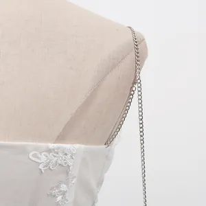 Vue détaillée d'une bretelle chaîne argentée sur une robe blanche dentelle brodée.