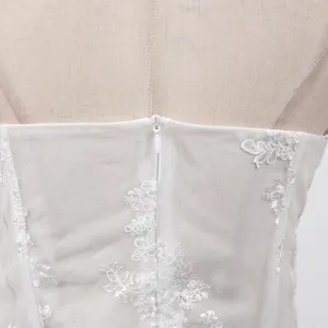 Gros plan d'une mini-robe en dentelle blanche avec broderie florale et fermeture éclair invisible.