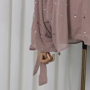 Detail of dusty rose long-sleeved top featuring shiny rhinestone embellishments and tie cuffs