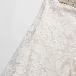 Close-up view of delicate white floral lace embroidery on a luxury vacation dress.