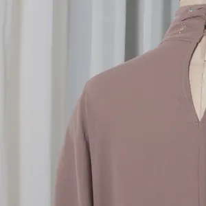 Macro detail view of an elegant high-neck mauve top with sparkly rhinestone embellishments.