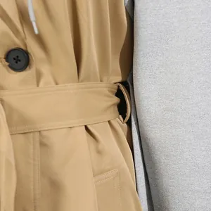 Makrodetail des camel Trenchcoats mit Taillenband und kontrastierendem grauem Kapuzenfutter.