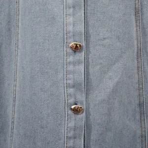 Detailaufnahme eines hellblauen Jeanskleids mit strukturiertem Stoff und goldenen Metallknöpfen