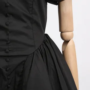 Close-up of black French style dress with covered buttons and pleated high waist detail.