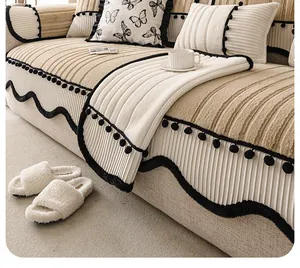 Détail de la housse de canapé en peluche crème avec bord noir ondulé et pompons