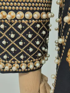 Macro view of pearl embellishments and gold pattern on a retro printed dress sleeve.