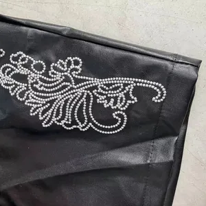 Detailed close-up of white traditional floral embroidery on black leather trousers
