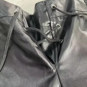 Detail of black faux leather shorts with silver eyelets and lace-up drawstring.