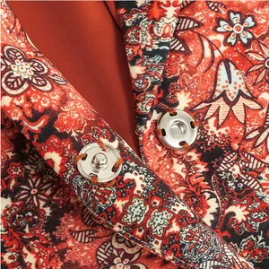Detailed view of silver snap buttons on an orange floral paisley print dress